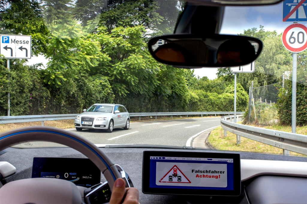 A wrong-way-driver-message is show to the driver in a vehicle. A car driving in the wrong direction is seen in the front.